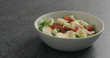 add olive oil to salad with mozzarella, cherry tomatoes and frisee leaves in white bowl on terrazzo surface