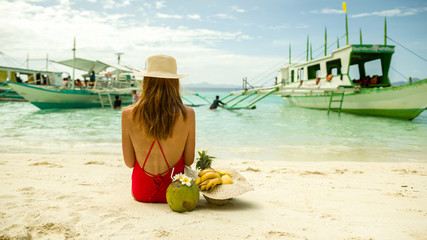 Young redhead vacation female in bikini and hat enjoying tropical fruits on bounty island - Banul beach, Coron, Palawan, Philippines