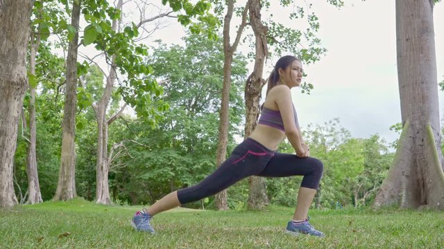 Young fit Asian woman stretching her body during her morning exercise at an outdoor nature park, healthy lifestyle