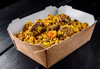 Rice with meat and vegetables in a box on on dark wooden tamle background