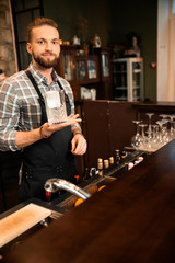 Smiling bartender holding glass with ice and looking at camera