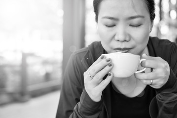 Asian girl smelling and enjoying cup of hot coffee at the outside of cafe. Black and white tone
