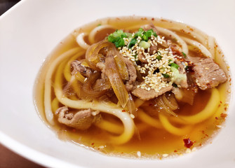 Buta Udon (Udon with braised pork) Udon noodle with pork and green leaf vegetable serving on white ceramic bowl. Japanese traditional food.