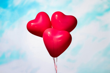 Fototapeta na wymiar man and woman hands holding three reds balloons in form of heart on the sky background in the blue pastel color. The concept of Valentines day.