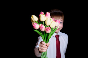 Cute boy in white shirt gives a bouquet of tulips. Isolate on black background