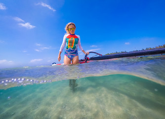 windsurfer girl with a board and a sail in tropical clear water, view from the waterline