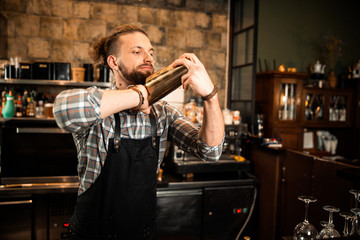 Young barman is holding a shaker at the bar