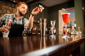 Young barman is holding a bottle of alcohol