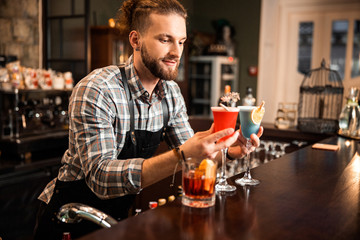Smiling bartender is holding two colorful cocktails