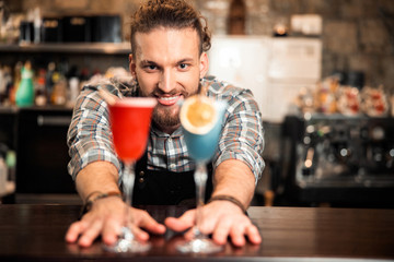 Smiling barman is looking on two colorful cocktails