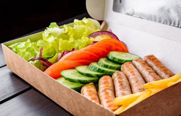 Sausage, French fries, Fresh vegetables mix in Delivery box on black table