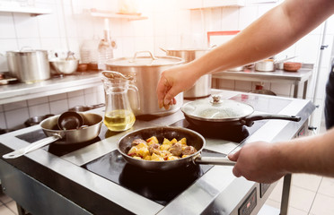 Chef cooks fried potatoes with pieces of meat in a restaurant kitchen