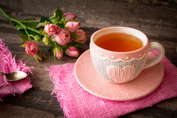 Close up of a cup of tea with roses and chocolate candies on wooden table