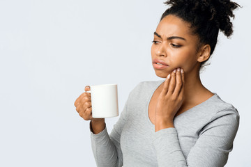 Afro girl suffering with sensitive teeth, drinking hot tea