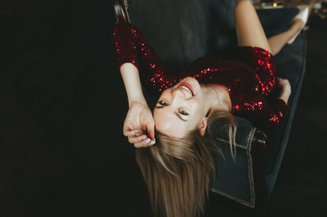 Fototapeta premium Young smiling beautiful blond woman in red dress sitting in an armchair. Top view