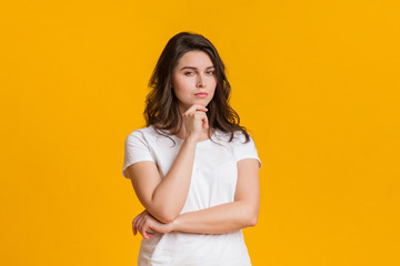 Sceptical young woman touching chin and looking suspiciously at camera