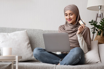 Muslim woman in headscarf with laptop and credit card at home