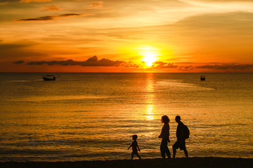 Silhouette of Sunset over the sea with a family walking on the beach at Khao Lak in Phang Nag, Thailand.