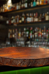 Wooden board on a background of bottles with alcohol. Old bar counter as layout for design. Workpiece for design. Empty place to advertise products. Blurred interior of the bar in the background.