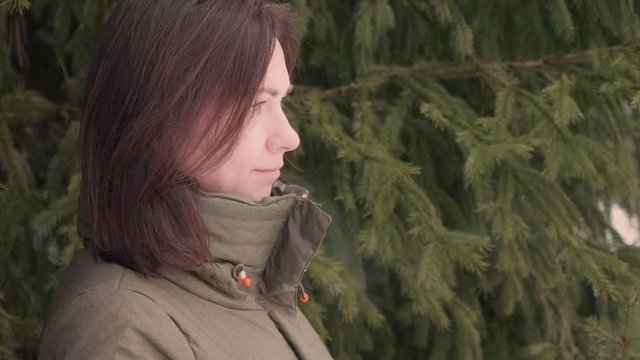 Side view of brunette with green furtree on background. Sad and thoughtful woman. Visible breath