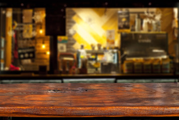 Wooden board on a background of bottles with alcohol. Old bar counter as layout for design. Workpiece for design. Empty place to advertise products. Blurred interior of the bar in the background.