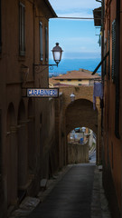 A narrow road/passage between two red brick walls in an old medieval Italian city with a beautiful view and Carabinieri (Police) sign on a wall