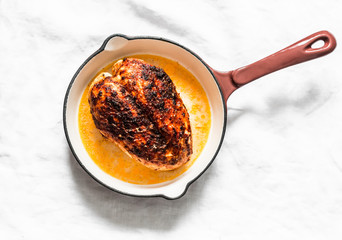 Simple roasted chicken breast in a cast iron pan on a light background, top view