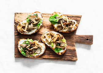 Mixed mushrooms cream cheese green salad on the grill bread sandwiches on a rustic cutting board on a light background, top view