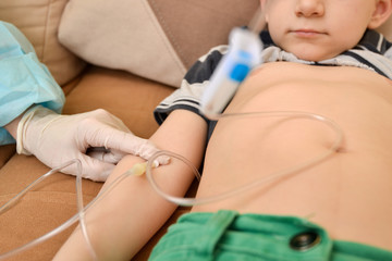 The doctor gives an injection to an ill child with an intravenous dropper at home.