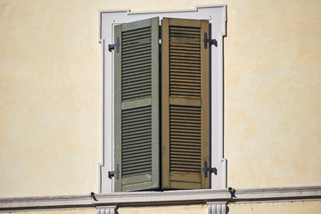 Italian window on the bright wall facade with closed wooden green shutters
