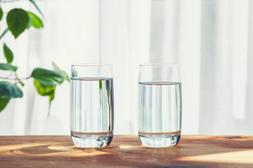 two glasses of water standing on wooden table inside, copy space