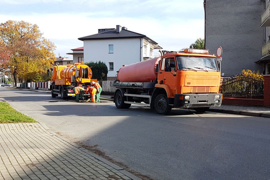 Sewage Clearing By Special Technical Means On The Streets Of A Small European Town. Orange Cars And Municipal Workers Clean The City From Debris And Dirt. Infrastructure