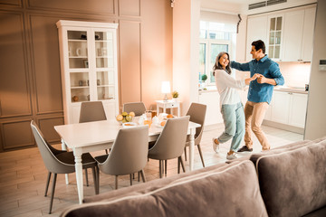 Happy beautiful lady dancing with her husband in living room