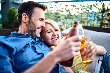 Picture of happy couple resting on patio together during summer day with beer and popcorn