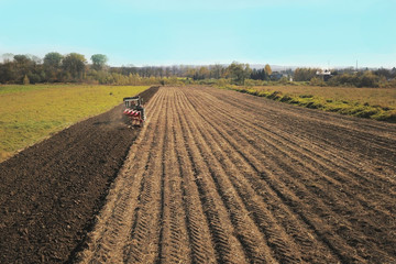 A farmer on a red tractor with a seeder sows grain in plowed land in a private field in the village area. Mechanization of spring field work. Farmer's everyday life. Processing of land. The agrarian
