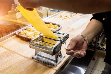 Chef rolling dough with a pasta machine. Pasta maker machine. 