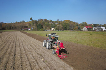 A farmer on a red tractor with a seeder sows grain in plowed land in a private field in the village area. Mechanization of spring field work. Farmer's everyday life. Processing of land. The agrarian
