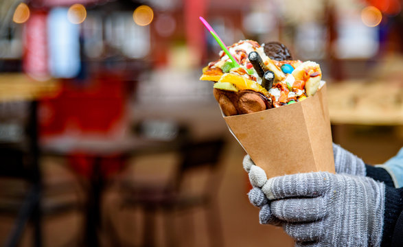 Young woman hands holding Hong Kong bubble waffle with ice cream, caramel syrup, fruits, chocolate 
