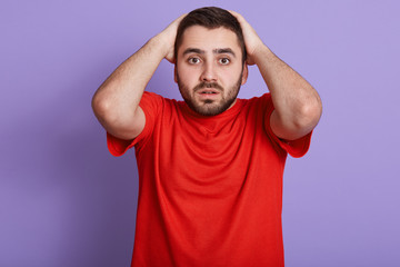 Fototapeta na wymiar Horizontal shot of young man looks stressed, unhealthy guy feeling pain in head, touching his head, isolated over purple studio background, bearded man having problems,does not know what to do.