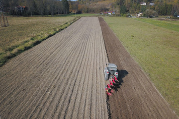 A farmer on a red tractor with a seeder sows grain in plowed land in a private field in the village area. Mechanization of spring field work. Farmer's everyday life. Processing of land. The agrarian