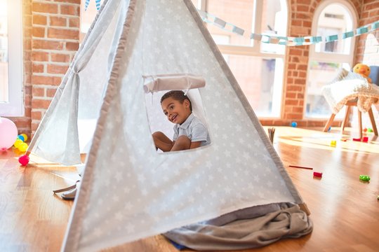 Beautiful african american toddler playing inside tipi smiling at kindergarten
