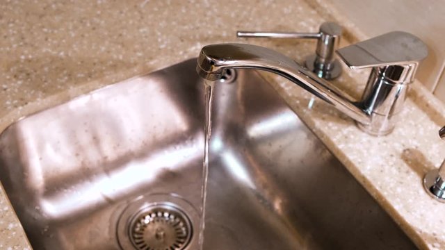 Water flows from the kitchen faucet into the metal sink. Concept. Clean water flowing from a chrome tap in the kitchen.