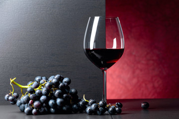 Blue grapes and glass of red wine on a black table.