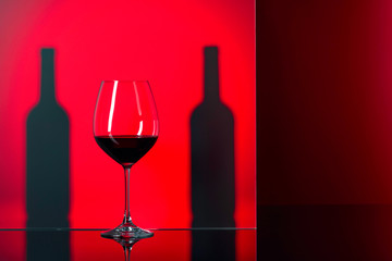 Bottles and glass of red wine on a red background.