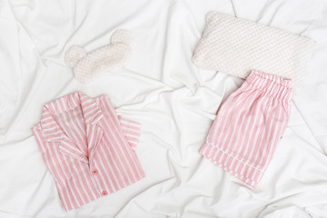 Sleepwear for slumber. Pink women pajama with stripes, shirt and shorts. Sleeping mask on white sheet. copy space. Top view. Flat lay.