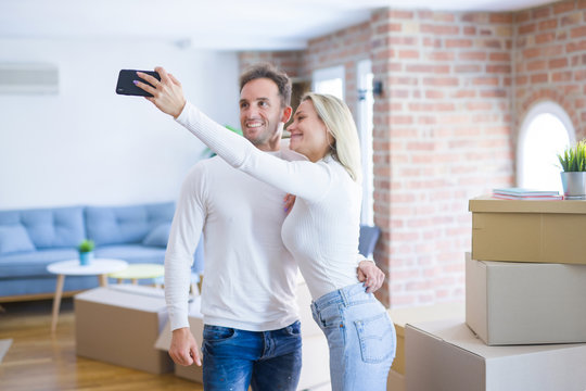 Young beautiful couple standing using smartphone to take selfie at new home around cardboard boxes - Powered by Adobe