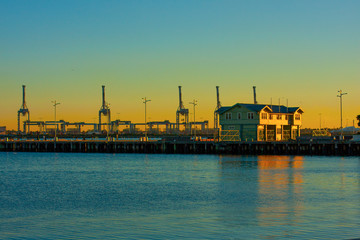 Obraz premium A pier in the port and port loading cranes in the distance against the beautiful sunset sky.