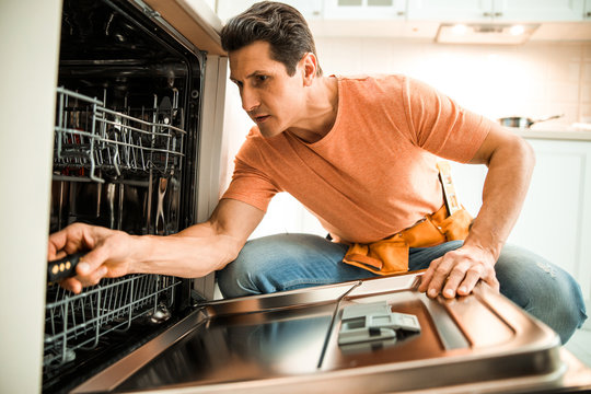 Adult man holding screwdriver to repair dishwasher on the kitchen