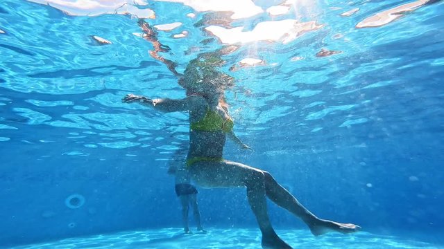 Underwater view of a young woman in a swimming pool. Woman in yellow swimsuit is swimming in the pool in summer.