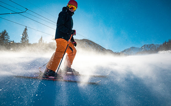 Skier on a slope standing still while snow flies around his legs and skis